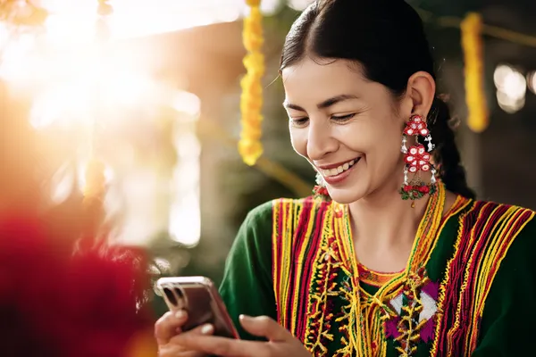 A cheerful woman in traditional clothing using her smartphone during a festive moment, showing how easily the RAJ123 app fits into everyday life.